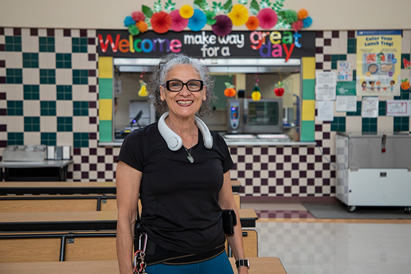 A woman wearing glasses and a black shirt smiles in the school cafeteria