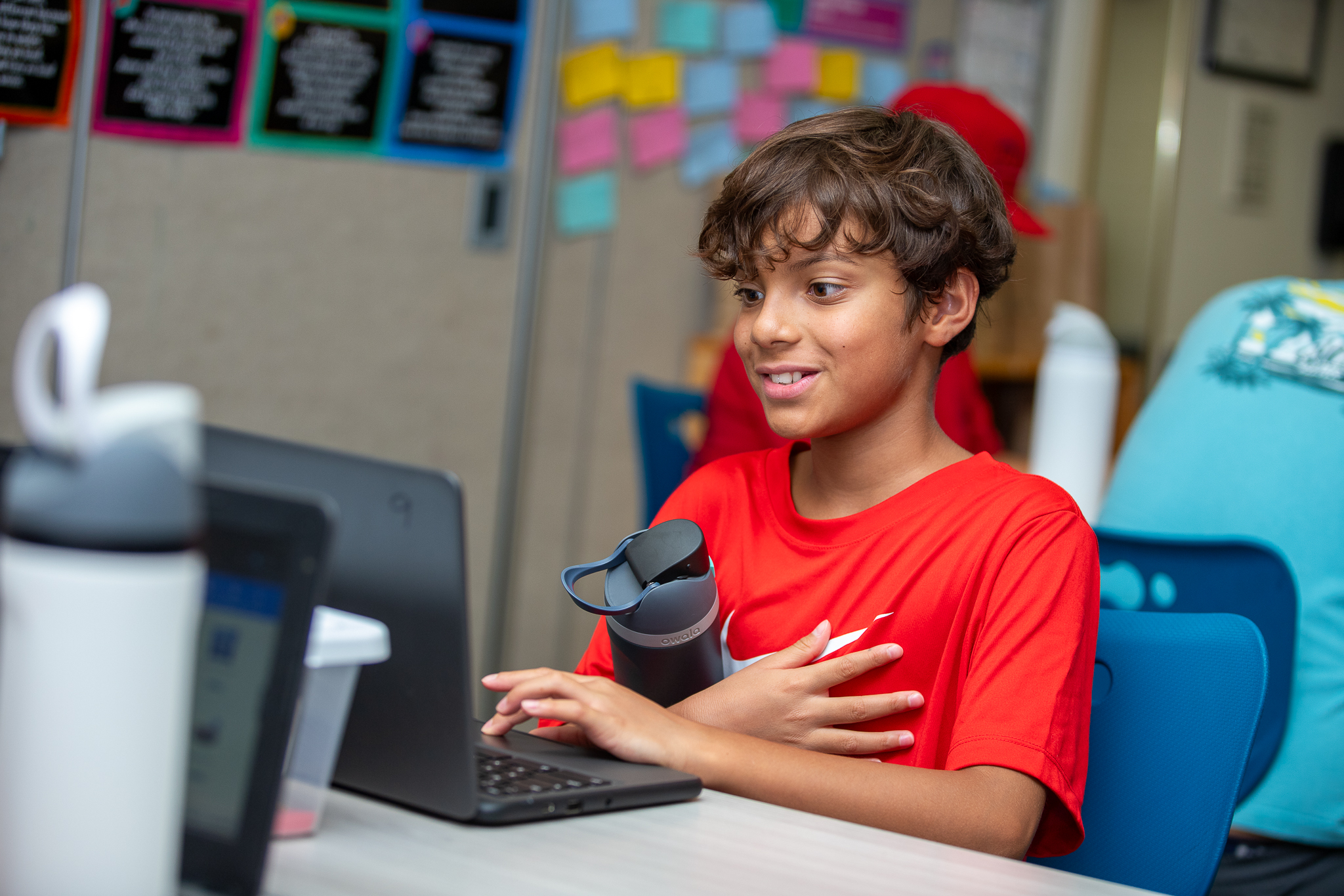 A boy holds his water bottle as he works on his Chromebook